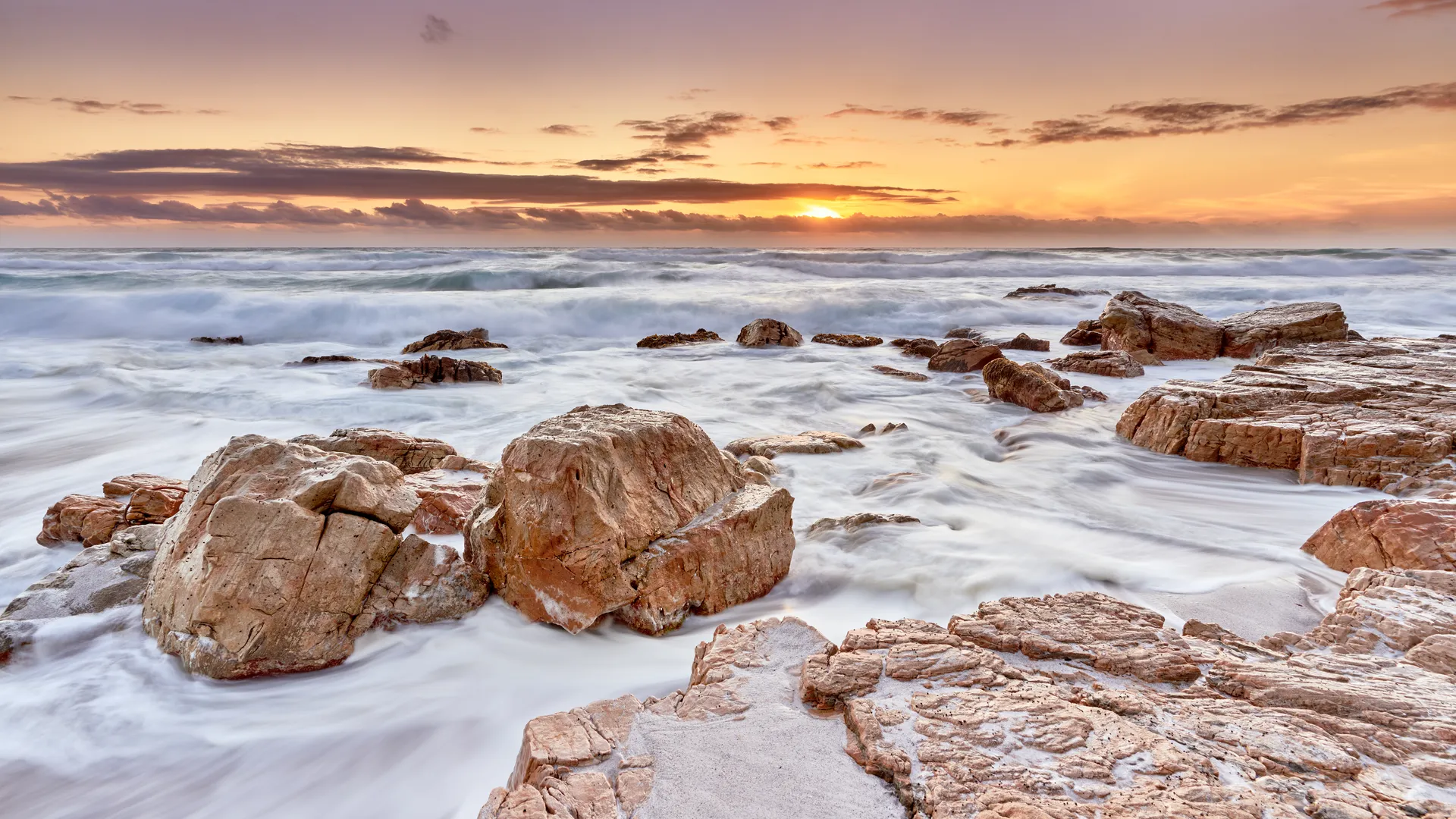 Powerful ocean waves breaking on a sandy beach at sunset with dramatic clouds, Misty Cliff, Cape Region, South Africa