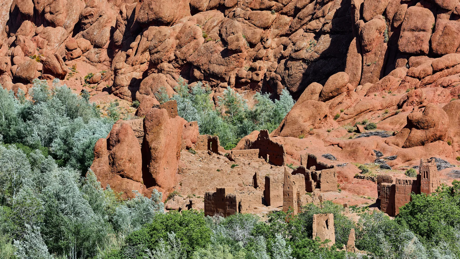 Ancient kasbah ruins nestled among red rock formations and green trees in Morocco